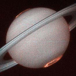 View of Saturn, with orange-brown auroral rings around each pole; image made by the Imaging Spectrometer on the Hubble Space Telescope using its UV band.