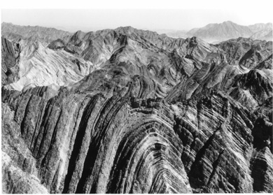 An aerial oblique photo showing the Zagros Mountains; note the cross-sectional appearance of an anticline exposed by a stream cut.